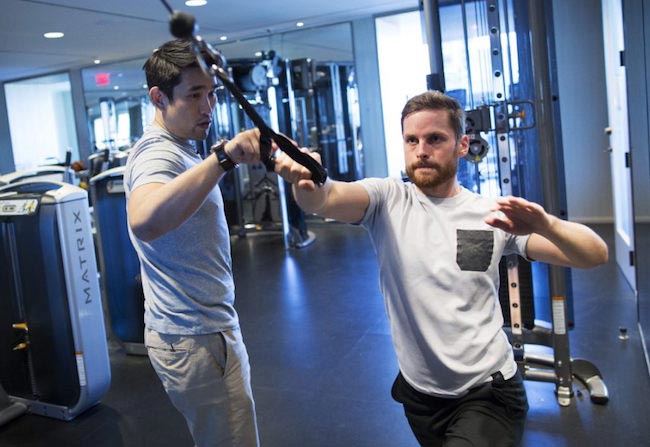 Dalton Wong guiding reporter Jonathan Forani through a combat pull cable machine