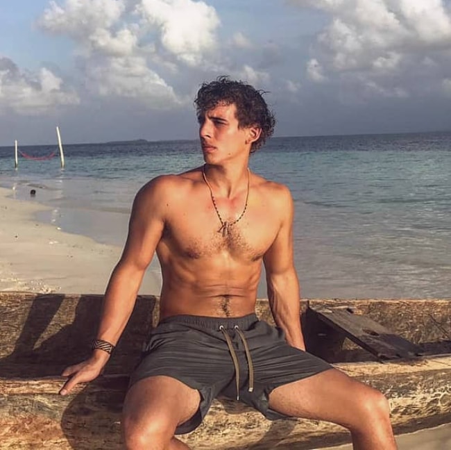 Miguel Herrán as seen shirtless while posing for a picture by a beach with a beautiful backdrop in April 2019