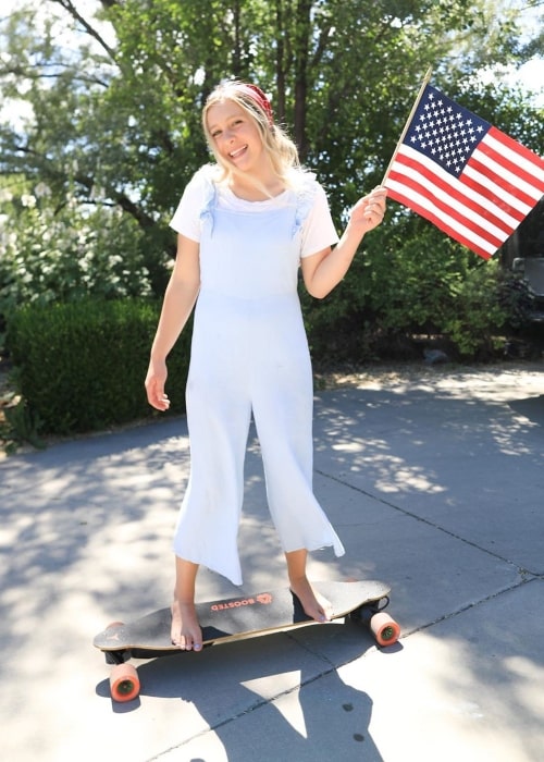 Taylor Shumway as seen in a picture taken while standing on a skateboard with the US flag in her hand and celebrating the 4th of July in the year 2020