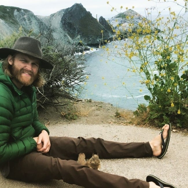Wyatt Russell smiling in a picture with a wild chipmunk posing between his legs in Big Sur, California in June 2019