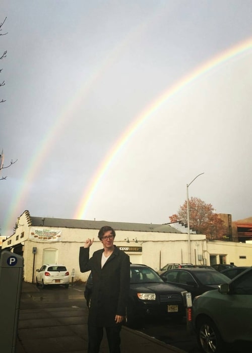 David W. Thompson posing for a picture with a backdrop of two rainbows at Peekskill Coffee in November 2016