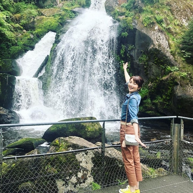 Megumi Sato posing for a picture in front of a waterfall