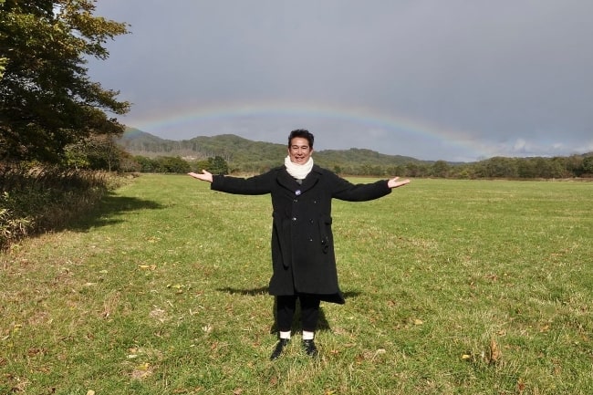 Takashi Ukaji posing for a picture with a rainbow in the backdrop in 2022