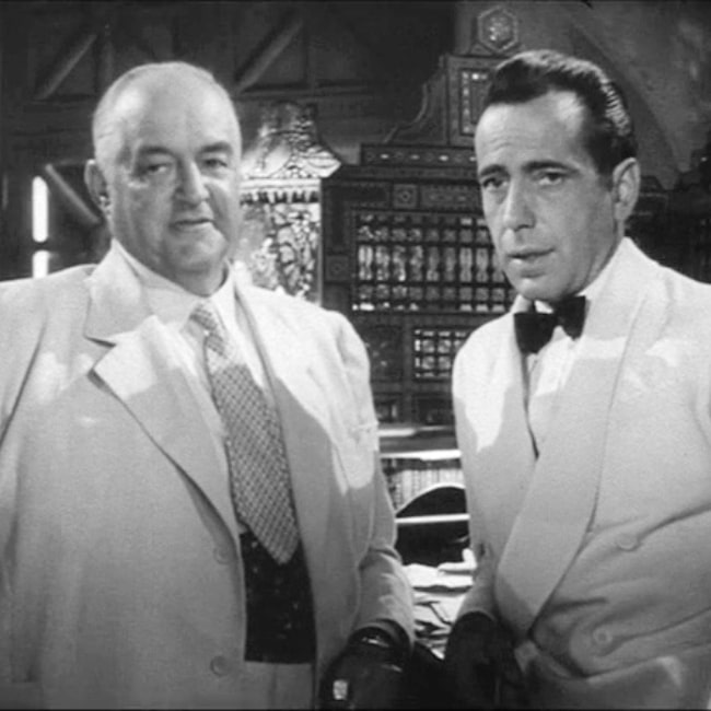 This screenshot shows Sydney Greenstreet and Humphrey Bogart in a discussion about whether Sam (Dooley Wilson) will come to work for Greenstreet in 1942