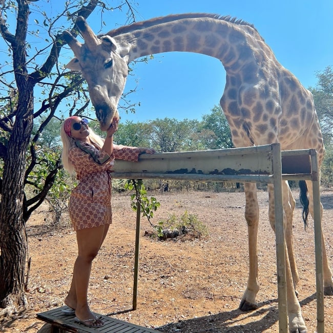 Boity Thulo posing for a picture with a giraffe at Avani Victoria Falls Resort in Zambia in 2023